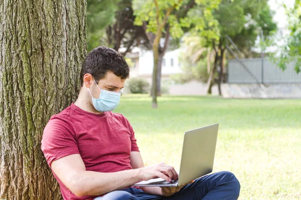 Yetişkinler parkta dizüstü bilgisayarla çalışıyor ve koruyucu maskeyle karşılaşıyorlar. Serbest Çalışan