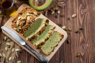 Arka planda avokado, petrol ve kabak çekirdeği ile bir ahşap kesme tahtası üzerinde Avocsdo ekmek dilimlenmiş