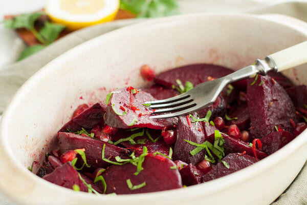 Roasted beets with pomegranate seeds and herbs on white wooden table 