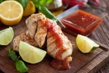 Baharatlı sos, taze fesleğen, limon ve ahşap kesme tahtası üzerinde limon ile servis ile mangalda tavuk fileto