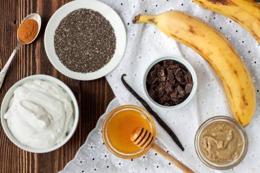 Puding, çikolata, muz, bal, chia tohum, baharat, vanilya, tarçın, ayçiçeği tohumu tereyağı rustik ahşap masa üzerinde. Chia puding için malzemeler