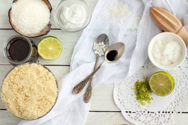 Badem unu, Hindistan cevizi kreması, kireç, baharat, akçaağaç sirup beyaz rustik masada. Ahşap kesme tahtası üzerinde çiğ vegan Hindistan cevizi ve kireç macaroons için malzemeler