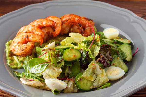 Delicious grilled shrimps served with salad with quail eggs and green vegetables - lettuce, cucumber. Healthy meal