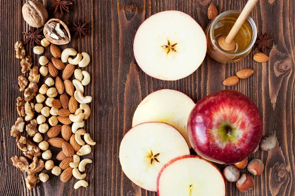 Sliced red apples, honey, cashew, almonds, walnuts, hazelnuts, anise stars on rustic wooden table