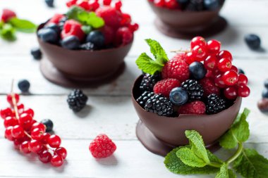 Ev yapımı tatlı koyu çikolata kase taze böğürtlen, ahududu, yaban mersini, frenk üzümü ve nane ile dolu beyaz tahta masada bırakır