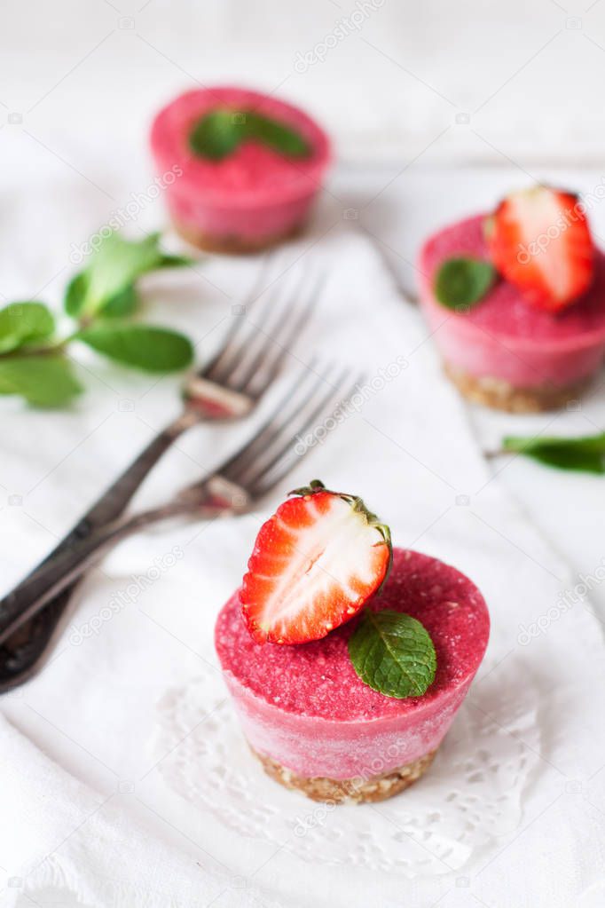 Vegan dessert - raw raw strawberry cheesecakes decorated with mint and fresh strawberries on white table