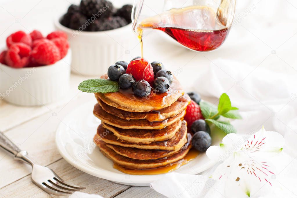 Stack of delicious paleo apple-cinnamon pancakes served with fresh berries, mint and maple syrup  