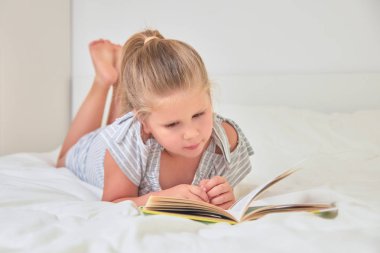 Sevimli küçük kız evde yatakta yatarken ve kitap okuma