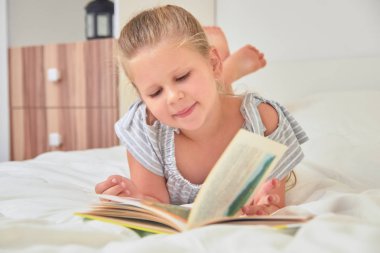 Sevimli küçük kız evde yatakta yatarken ve kitap okuma