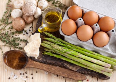 Taze mantar, kuşkonmaz, yumurta, Parmesan peyniri, zeytinyağı, kekik, su ahşap arka plan üzerinde. Lezzetli frittata kuşkonmaz ve mantar için malzemeler 