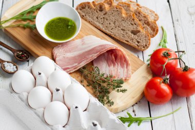 Lezzetli domuz pastırması ve yumurta kek için malzemeler. Çiğ yumurta, pastırma dilimlerini, ekmek, domates, sos pesto, Yeşiller ve baharat ahşap adam üzerinde