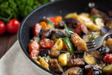 Kavrulmuş kabak, patlıcan, domates, baharat ve tavada ahşap masa üzerinde taze fesleğen