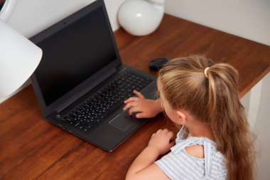 Dizüstü bilgisayar kullanan küçük kız evde masanın odaklı