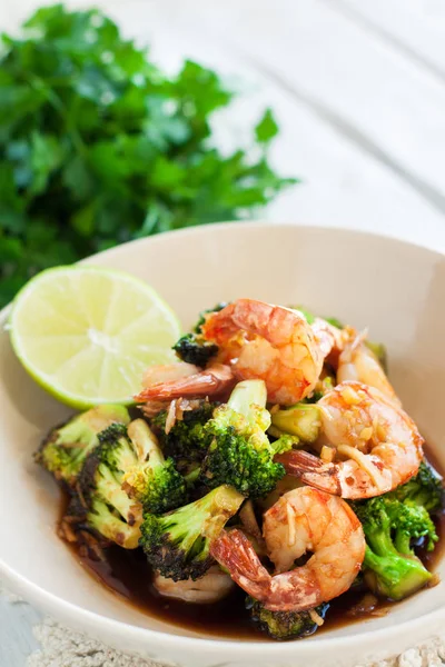 Roasted shrimps with broccoli and honey and garlic sauce served with lemon and greens on wooden table