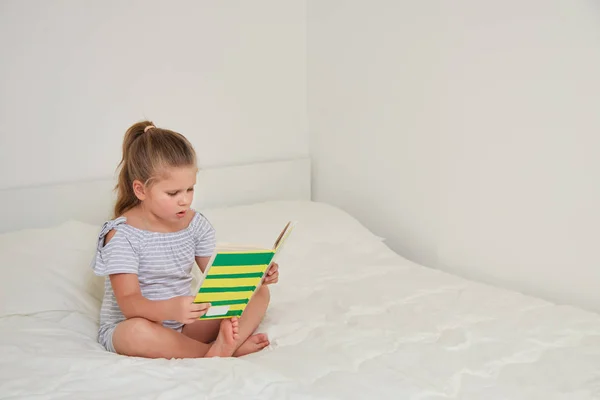 Маленькая Блондинка Читает Сказки Сидя Позе Лотоса Кровати Своей Комнате — стоковое фото