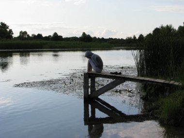 Sessiz bir akşam. Nehir. Sazlıklarla dolu durgun su. Tekneler için ahşap iskele. Kafası aşağıda bir kız iskelede oturuyor. Çok yalnız ve üzgün..