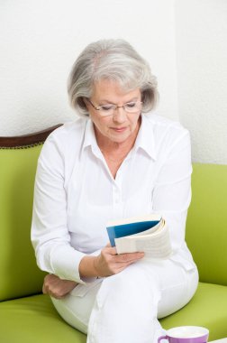 Kanepede oturup kitap okuyan olgun bir kadın.