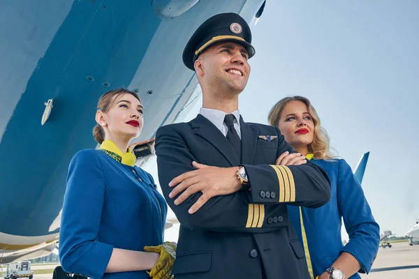Álomszerű stewardessek állnak a pilóta mögött összecsukott karokkal — Stock Fotó