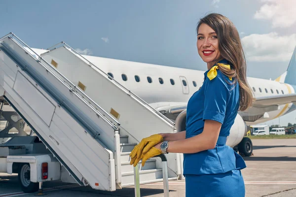 Hospedeira feliz em pé na frente do avião — Fotografia de Stock