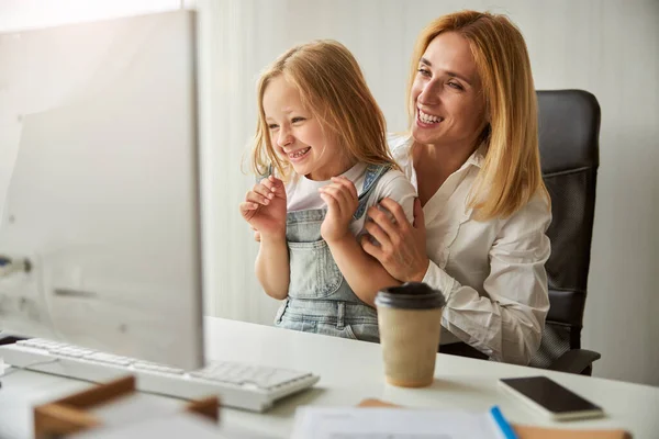 Attractive blonde Caucasian woman hugging little girl while spending time in the office — Stock Photo, Image