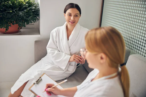 Kurgast sitzt auf dem Sofa neben einer Kosmetikerin — Stockfoto