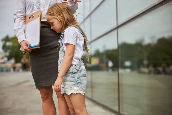 Smutna piękna córka ubrana w dżinsowy romper stojąca blisko matki — Zdjęcie stockowe