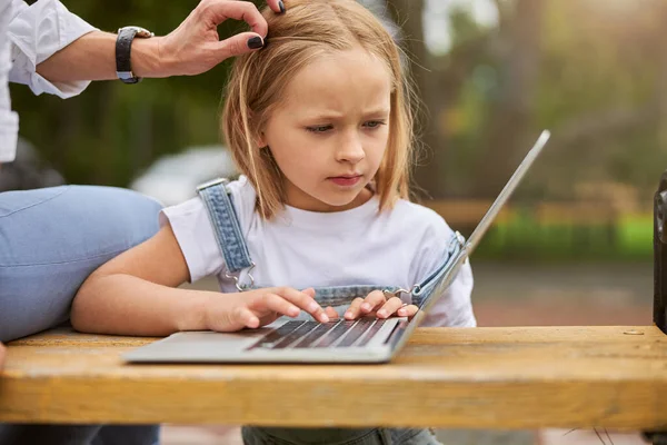 Portrét půvabné soustředěné dívky na lekci na notebooku v parku s mámou — Stock fotografie