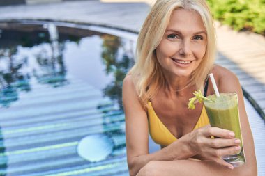 Elinde meyve suyuyla gülümseyen kadın fotoğraf makinesine bakıyor.