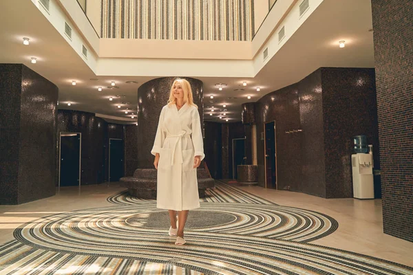 Mujer vestida de blanco suave albornoz de pie en el salón del hotel spa —  Fotos de Stock