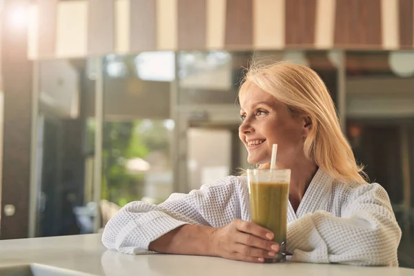 Vrolijke vrouw in witte badjas met glas sap terwijl weg te kijken — Stockfoto