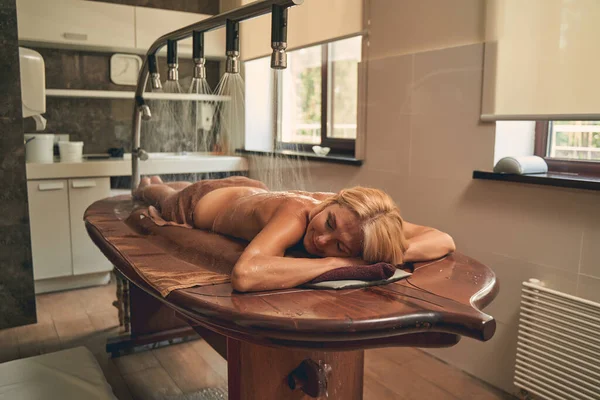 Спокойная женщина лежит на деревянном столе в ванной комнате — стоковое фото