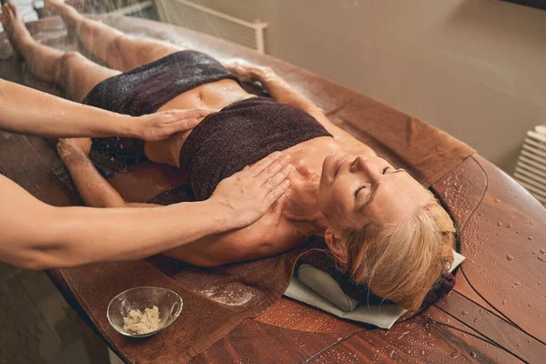 Senhora alegre relaxante na mesa de madeira na terapia de massagem — Fotografia de Stock