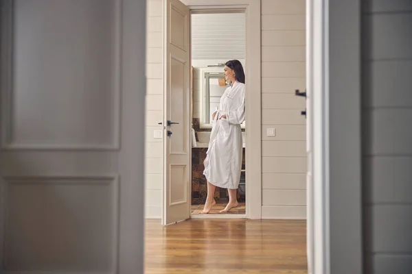 Красивая дама в белом мягком халате стоит в ванной комнате — стоковое фото
