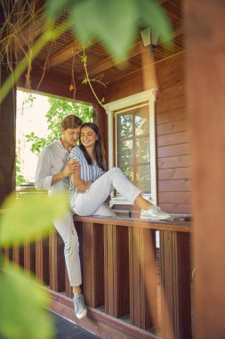 Yakışıklı bir adam ve beyaz pantolon giyen çekici bir kadın verandada yan yana otururken gözleri kapalı.