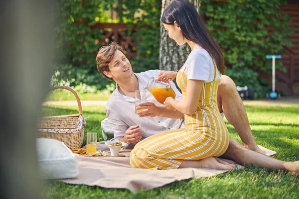 Веселая леди наливает апельсиновый лимонад в бокал для своего любимого мужчины — стоковое фото