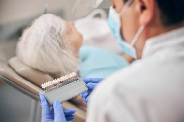 Diş beyazlatma kliniğinde diş rengi paleti tutan erkek dişçi.