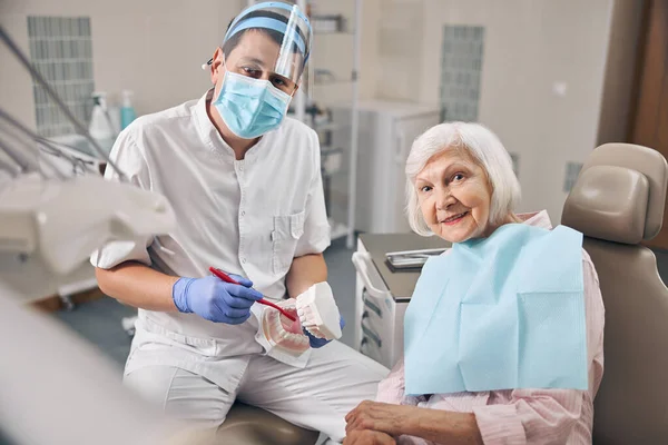 Jeune médecin en uniforme parle de l'hygiène des dents dans le cabinet dentaire — Photo