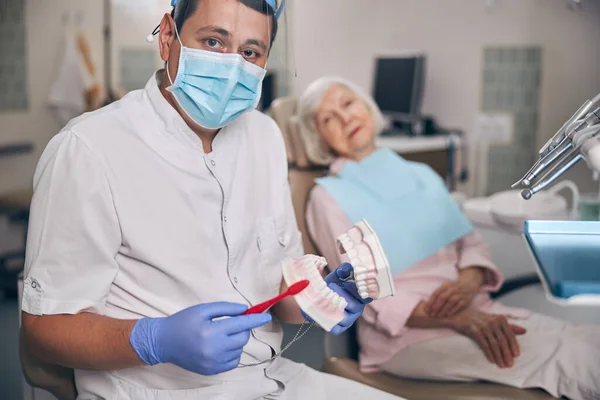 Jeune beau orthodontiste et patiente assise dans une clinique dentaire — Photo