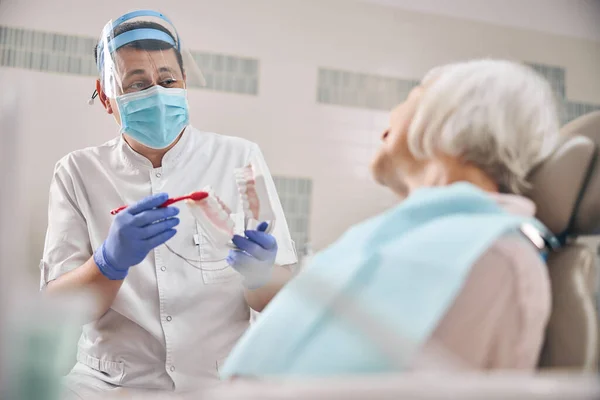 Γυναίκα οδοντίατρος μιλάει με ασθενή, ενώ δείχνει οδοντιατρική σαγόνι μοντέλο στην οδοντιατρική κλινική — Φωτογραφία Αρχείου