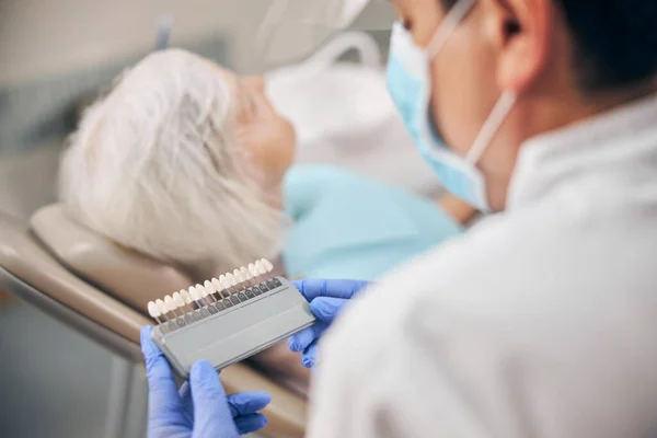 Dentiste masculin tenant dans la palette de couleurs de la main pour le blanchiment dans la clinique dentaire — Photo