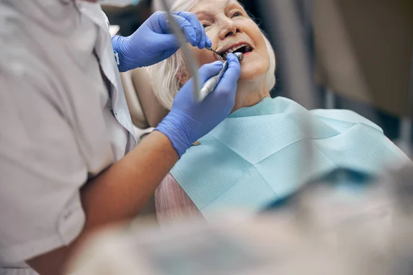Male dentist treating teeth to senior woman patient in clinic — Stock Photo, Image