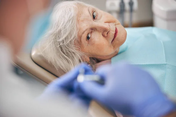 Összpontosított fehér nő nézi az orvos kezét fogorvosi felszereléssel — Stock Fotó