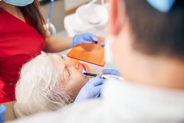 Rijpere arts met verpleegkundige werken met patiënt in de tandheelkundige kliniek — Stockfoto