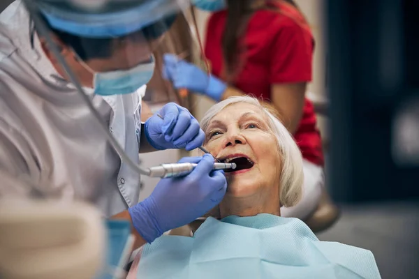 Volwassen mannelijke tandarts doet tandheelkundige ingrepen van de patiënt op het tandartspraktijk — Stockfoto