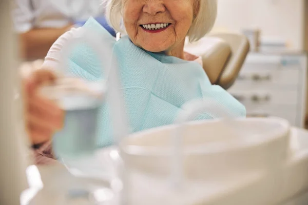 Smiling female sitting on the dentist chair while having care to the teeth — Stock Photo, Image