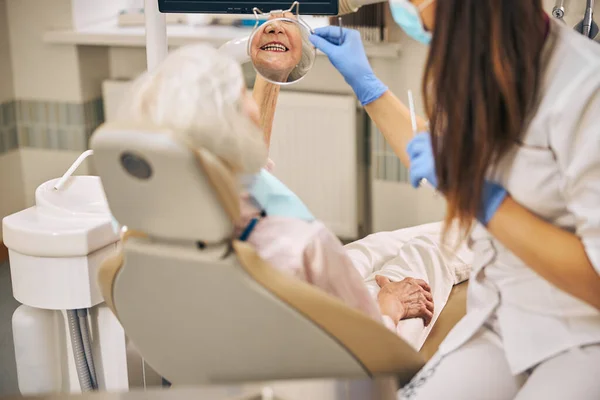 Vrouwelijke tandarts onderzoeken tanden met behulp van spiegel in tandheelkundige kliniek — Stockfoto