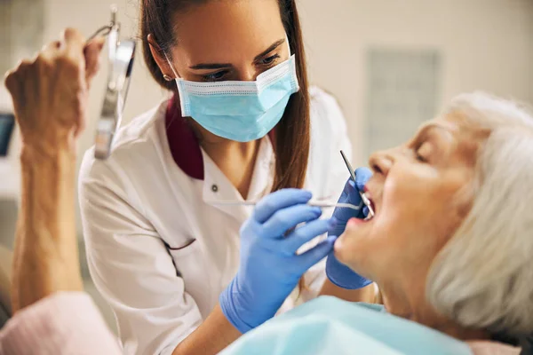 Portret van vrouwelijke tandarts die tanden van oudere patiënte behandelt — Stockfoto