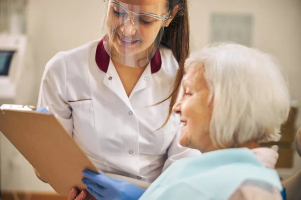 Happy smiling patient of dental clinic looking at the clipboard — Stock Photo, Image