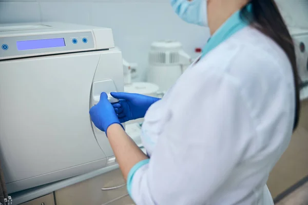 Žena v bílé uniformě a modrých rukavicích pracující s moderním strojem ve stomatologii — Stock fotografie