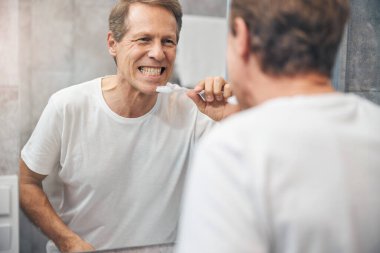 Adam aynada sıkılmış dişlerine bakıyor.